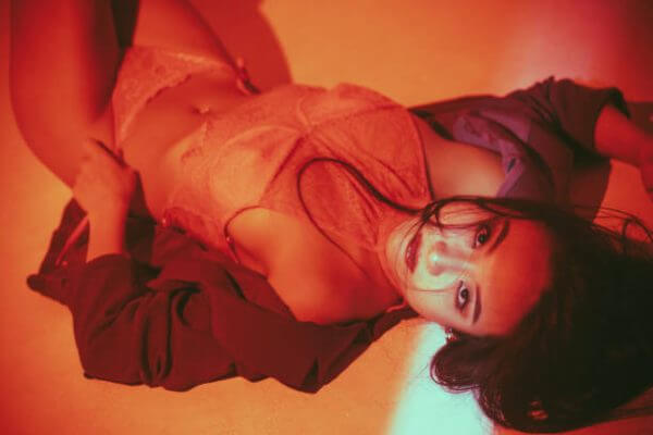 Asian woman in red lingerie lying under warm red lighting, creating a sensual and artistic atmosphere.